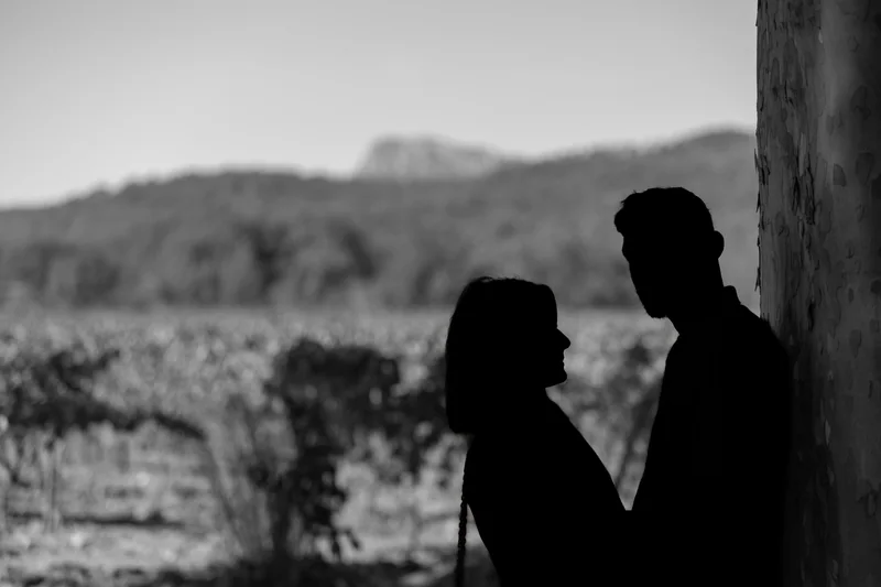 Deux silhouettes se font face devant un paysage de vignes, en noir et blanc.