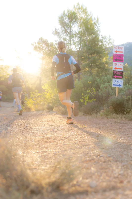 Des coureurs avancent sur un sentier poussiéreux à contre-jour.